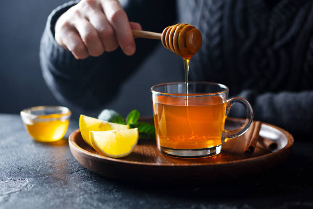 Cup of tea with pouring honey and lemon. Grey background.